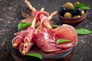 A wooden board with some meat and olives on it