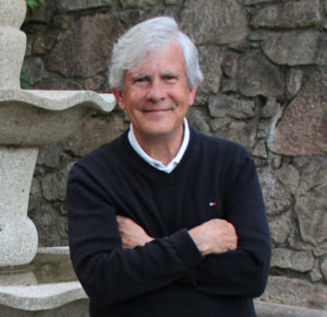 A man with his arms crossed standing in front of a stone wall.