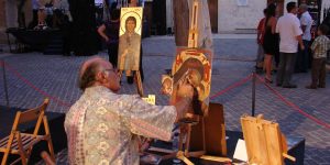 A man painting on canvas with some people in the background