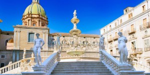 A fountain with statues on the steps of an old building.