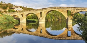 A bridge with two arches is reflected in the water.