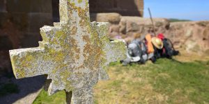 A cross with moss growing on it in front of some people.