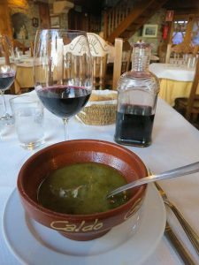 A bowl of soup on the table with wine.