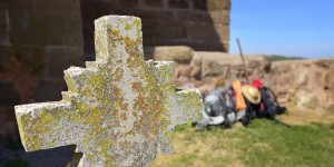 A cross is in the foreground with other people and items behind it.