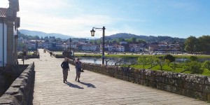 Two people walking on a sidewalk near the water.