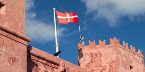 A red flag flying on top of a pink wall.