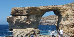 People are standing on the rocks near a rock arch.