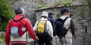 A group of people with backpacks walking on the side of a stone wall.
