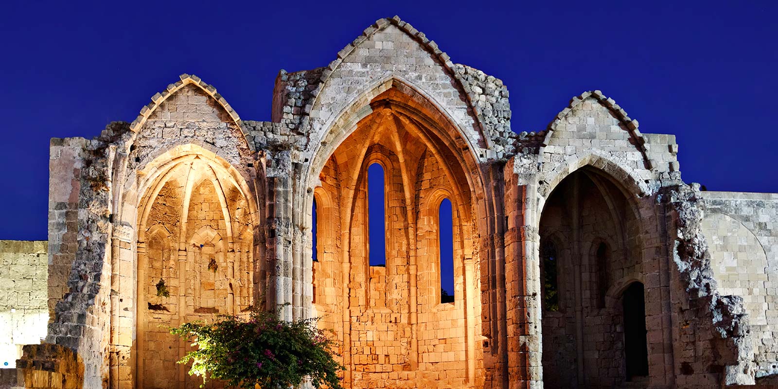 A stone building with arches and windows lit up at night.