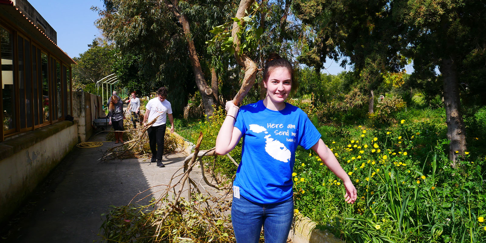 Young adult helping to clean up branches and brush during Camino trip.