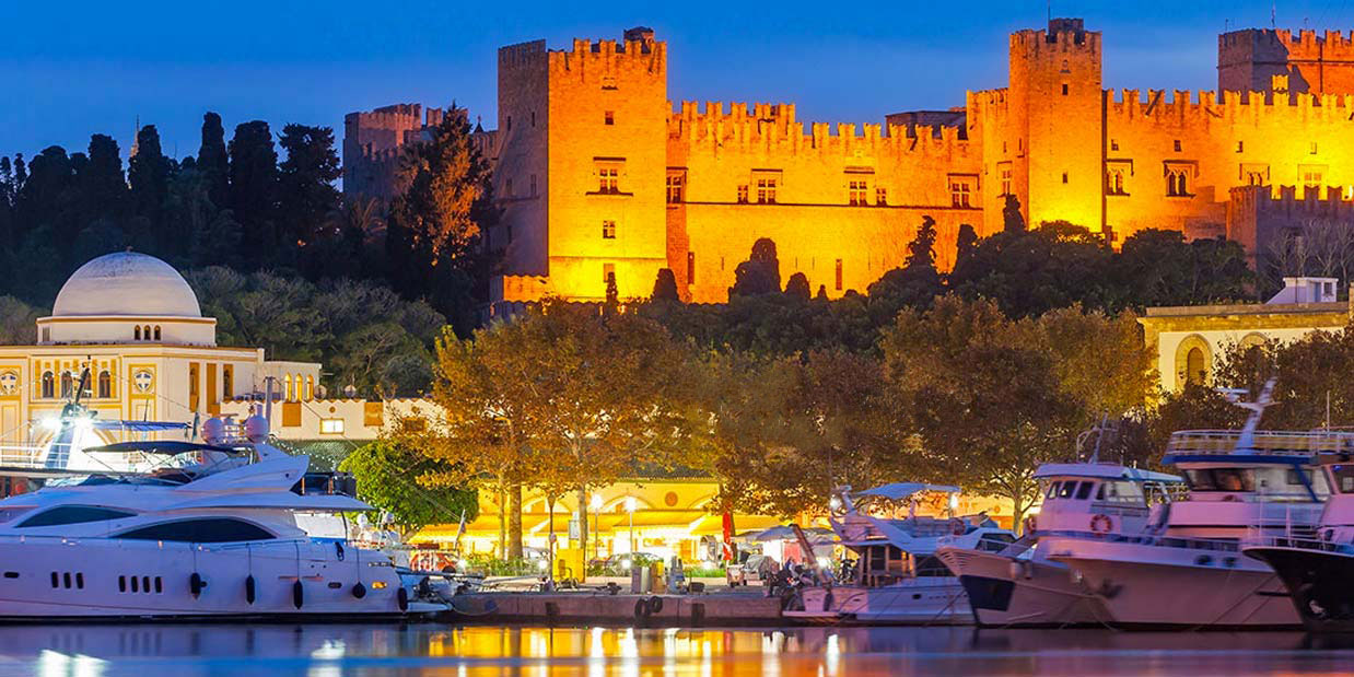 Night image of a castle with water and boats docked in the foreground.