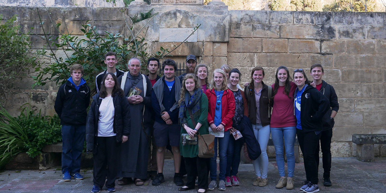 Students from MedSeas Malta Misson trip pose with priest in front of Catacombs